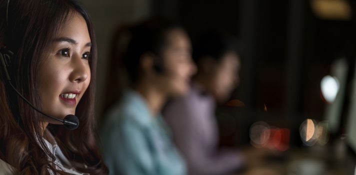 Portrait of Asian Female customer care service with business man smiling and working hard late in night shift at office,call center department,worker and overtime,teamwork with colleagues for success