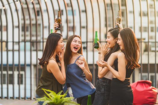 Happiness Asian Girl Friend Group celebrating and dancing together with her beer bottle at sunset time on rooftop of downtown hotel or nightclub,hens night,holiday, or yearly anniversary party concept