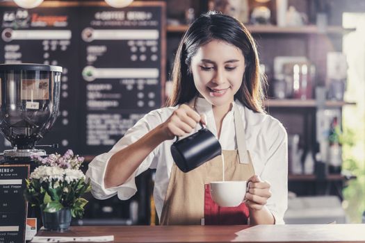 Asian Barista preparing cup of coffee, espresso with latte or cappuccino for customer order in coffee shop,bartender pouring milk,Small business owner and startup in coffee shop and restaurant concept