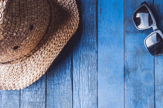 Hat with sunglasses on blue painted wood plank background. Free space for text