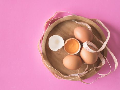 Eggs with tape measure on pink background.