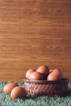 Eggs in wooden basket on green grass. Free space for text