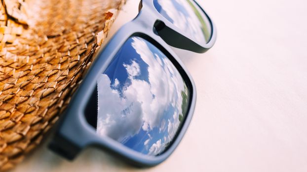 Sunglasses with the reflection of  blue sky and hat on the table, Soft focus.