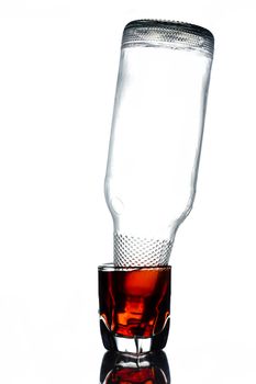 Glass of alcohol with empty bottle on a white background.