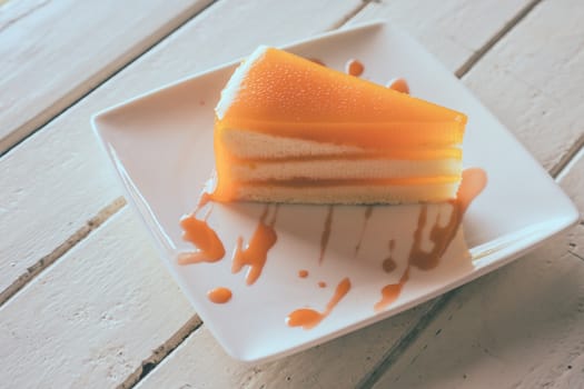 Orange cake in white dish on the wooden table.