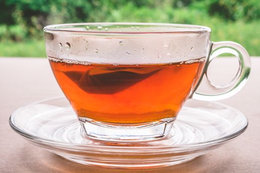 A cup of tea on the wooden table, tea bag in glass, nature background.