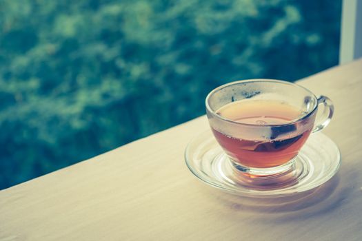 A cup of tea on the wooden table, tea bag in glass, nature background. Vintage tone. Free space for text