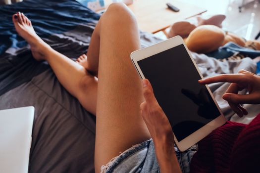 Close up of young woman using tablet while sitting on her bed,  Films grain filter.