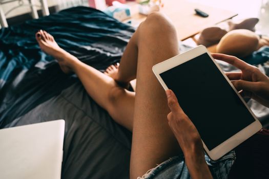 Close up of young woman using tablet while sitting on her bed,  Films grain filter.