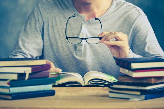 Close up of a man holding eyeglasses and reading a book on the wooden table. Vintage tone