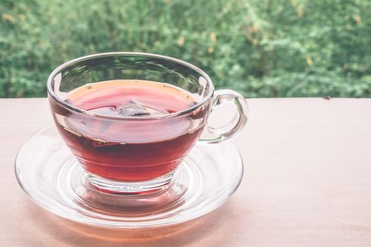 A cup of tea on the wooden table, tea bag in glass, nature background.