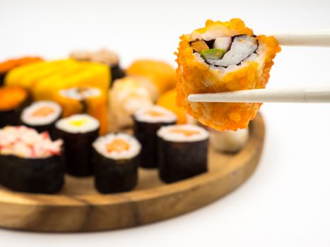 Hand holding sushi roll with chopsticks, Sushi set on wooden plate background, Japanese food.