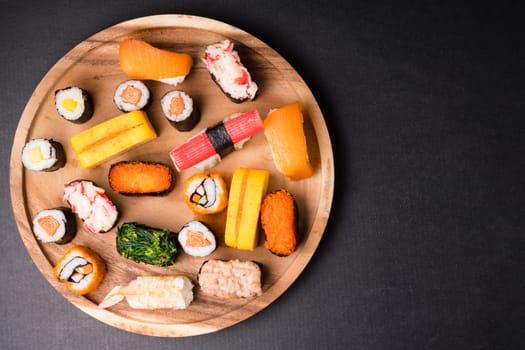 Top view of Sushi set on wooden plate on black background, Japanese food. Free space for text