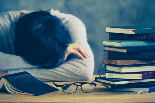 Tired young man sleeping with book stacks on the wooden table. Vintage tone