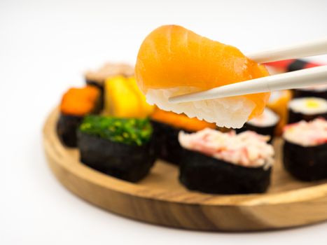 Hand holding sushi with chopsticks, Sushi set on wooden plate background, Japanese food.