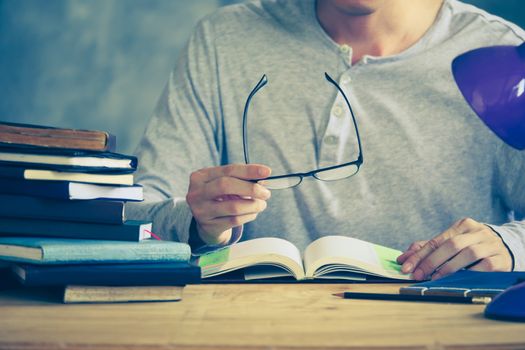 Close up of a man holding eyeglasses and reading a book on the wooden table. Vintage tone