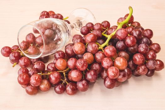 Red grapes with wine glass on the wooden table.