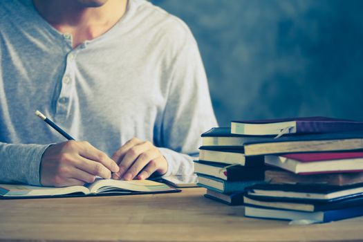 Close up of a man writing in notebook, Stack of old books on wooden desk. Vintage tone