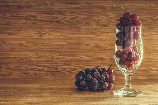 Red grapes in glass on the wooden table. Free space for text