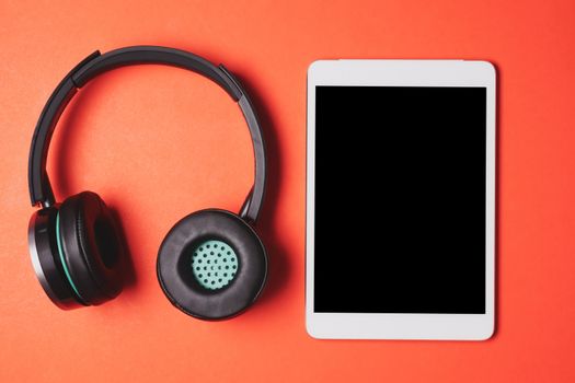 Modern headphones with tablet pc on a orange background.
