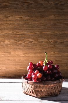 Red grapes in basket on the wooden table. Free space for text