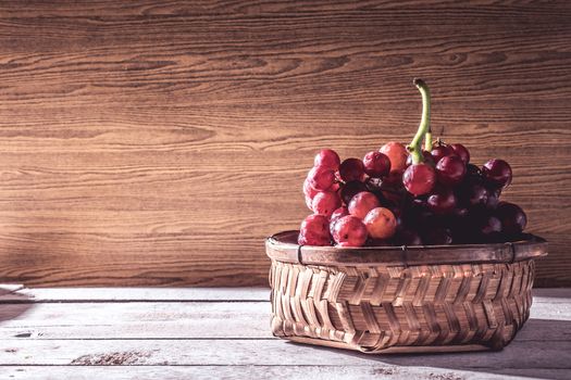 Red grapes in basket on the wooden table. Free space for text