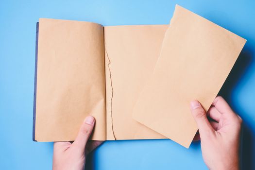 Top view of hands tear paper in notebook on blue background.
