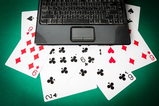 Laptop with playing cards on green background.