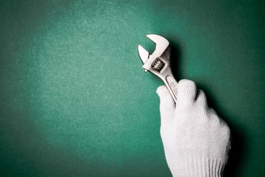 Wrench in hand with protection glove on green background. Free space for text