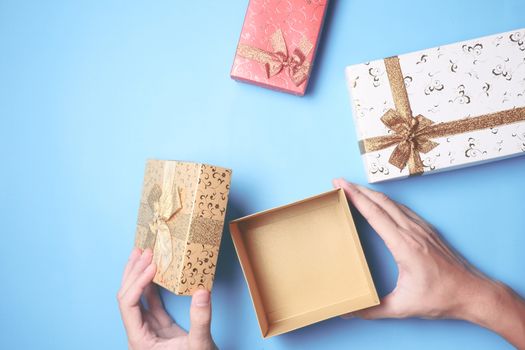 Top view of male hands opening a gift box, presents on blue background.