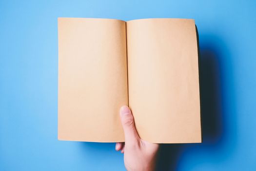 Top view of hands holding a blank book ready with copy space ready for text on blue background.
