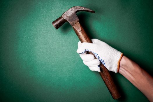 Hammer in hand with protection glove on green background. Free space for text