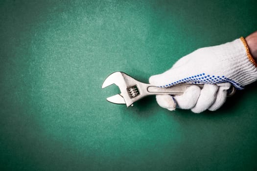 Wrench in hand with protection glove on green background. Free space for text