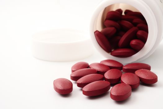 Red vitamin pills pouring out of the bottle on white background.