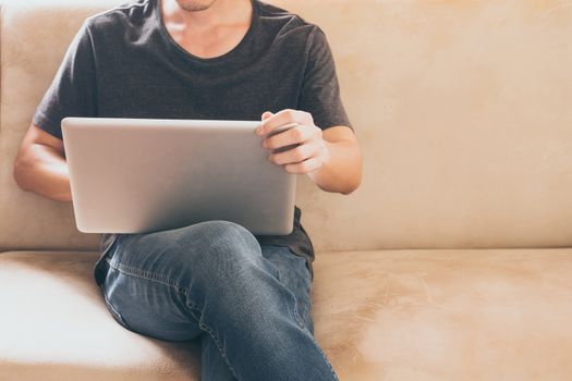 Close up of casual young man sitting on sofa and using a laptop at home.