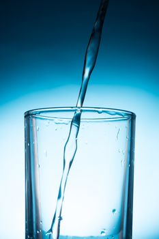 Pouring water into glass on blue background.