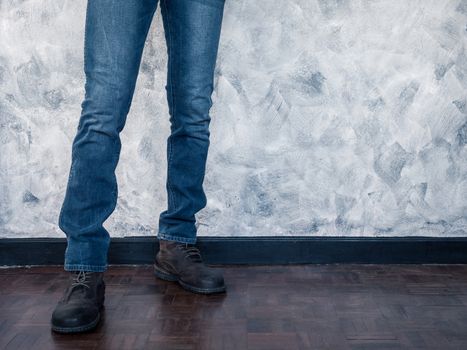 Close up of Man's legs in jeans and boots on wooden floor. Free space for text