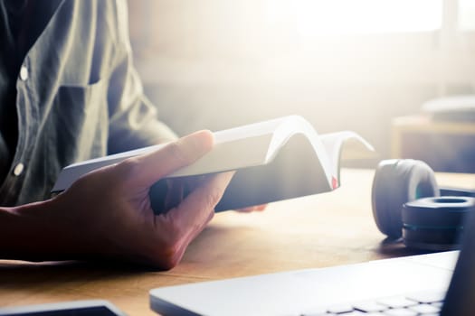 Close up of casual man reading a book on the desk at home, toned with sunlight