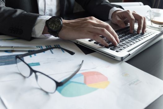 Close up of Businessman using laptop and analyzing investment charts on the office desk.