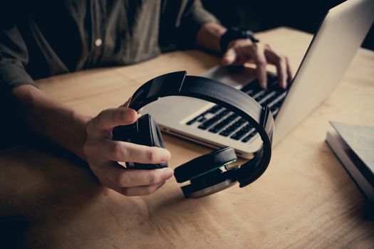 Close up of casual man holding headphones and using laptop on the desk at home.