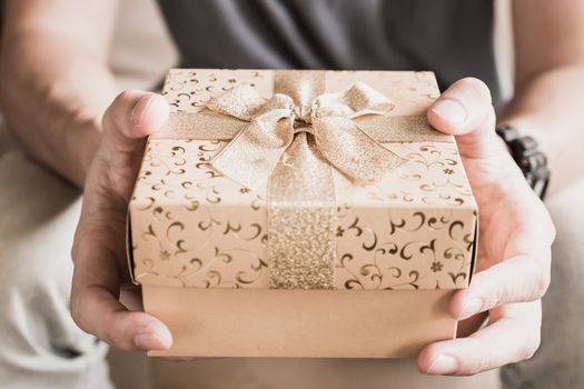 Close up of male hands holding golden gift box.
