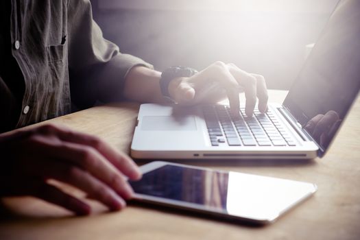 Close up of Male hands using laptop and tablet on the table, toned with sunlight