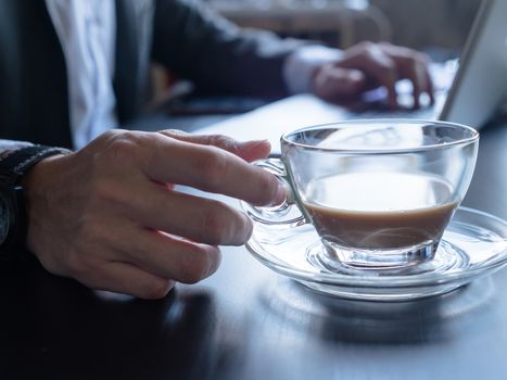 Close up of Businessman drinking coffee and using a laptop on the office desk.