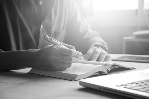 Close up of casual man writing note and using laptop on the desk, toned with sunlight