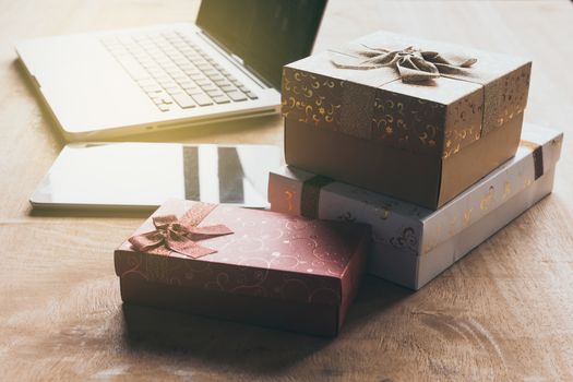 Laptop with tablet and gift boxes on wooden table.