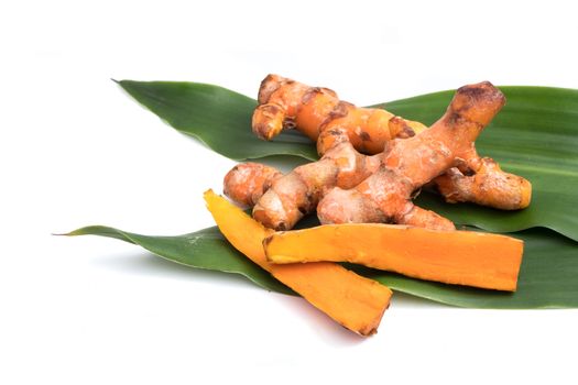 Turmeric roots on green leaf over white background.