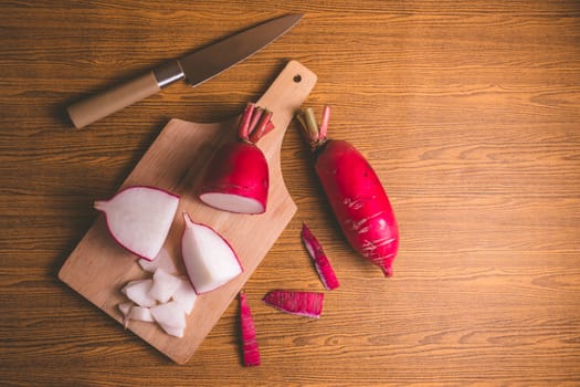 Fresh Pink Radishes on wooden cutting board over wooden table background.