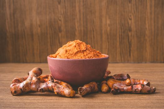 Turmeric roots with turmeric powder on wooden background.