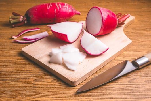 Fresh Pink Radishes on wooden cutting board over wooden table background.
