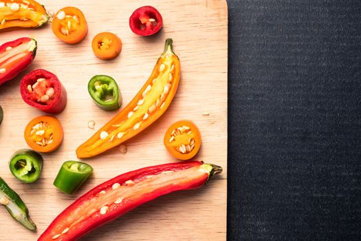 Colorful mix of chili pappers on wooden tray over black background. Free space for text